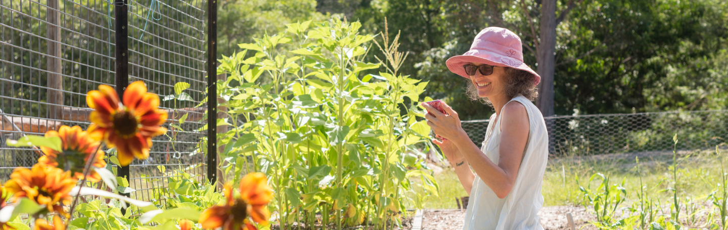 Woman using her mobile phone while kneeling in her garden